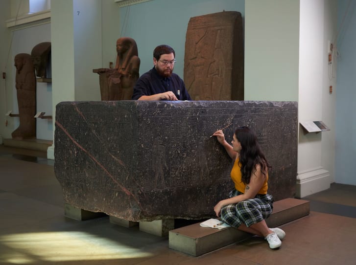 Senior Conservator Stephanie Vasiliou (left) and former conservation student Shoun Obana (right) clean "The Enchanted Basin," sarcophagus of Hapmen, 600 BC, on display at The British Museum.